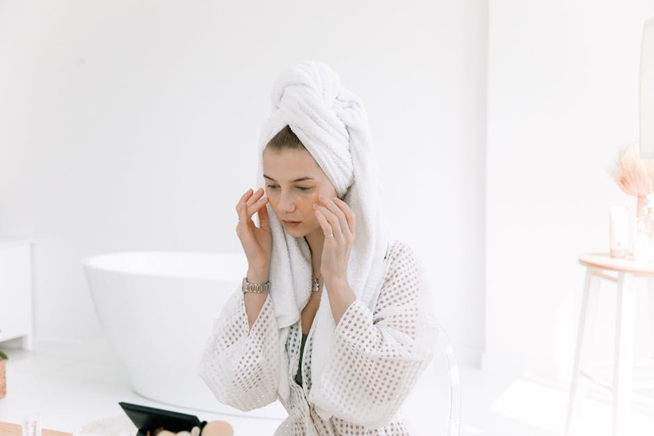 Woman in white bathrobe applying skincare in a bright bathroom. Perfect for wellness and beauty themes